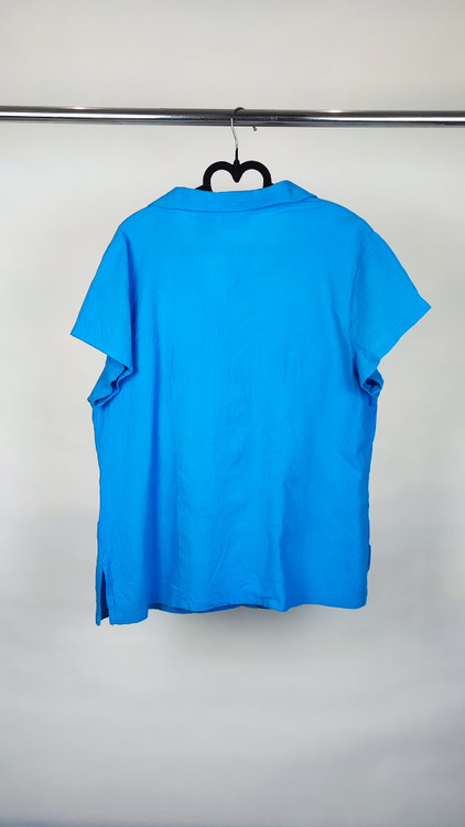 زن با شومیز آبی روشن آستینکوتاه و دکمهدار، دارای یقه برگردان، ایستاده در پسزمینه روشن