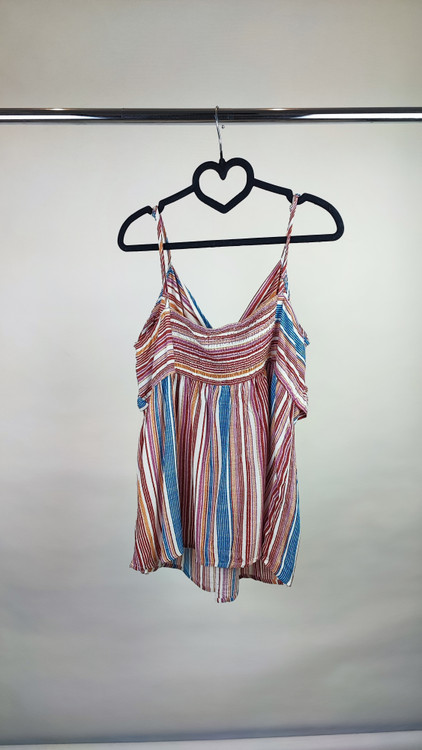 زن با تاپ بندی طرحدار راهراه با رنگهای صورتی، طوسی و سفید، یقه هفت و فرم آزاد، همراه با شلوار جین تیره در پسزمینه روشن ایستاده است.»