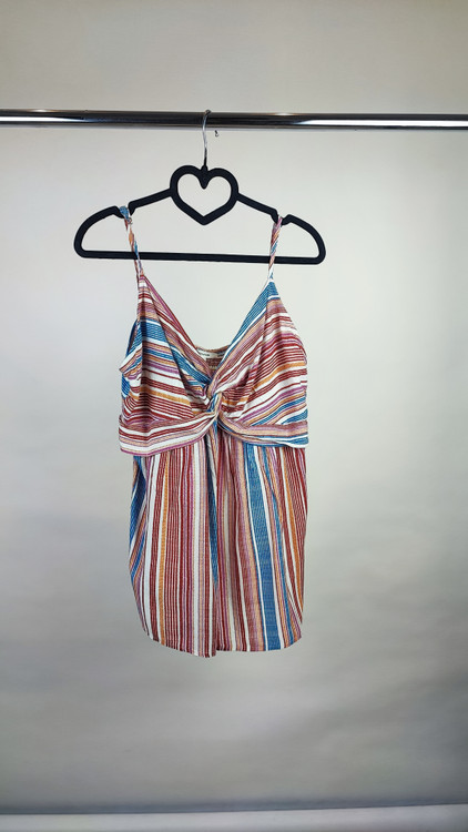 زن با تاپ بندی طرحدار راهراه با رنگهای صورتی، طوسی و سفید، یقه هفت و فرم آزاد، همراه با شلوار جین تیره در پسزمینه روشن ایستاده است.»