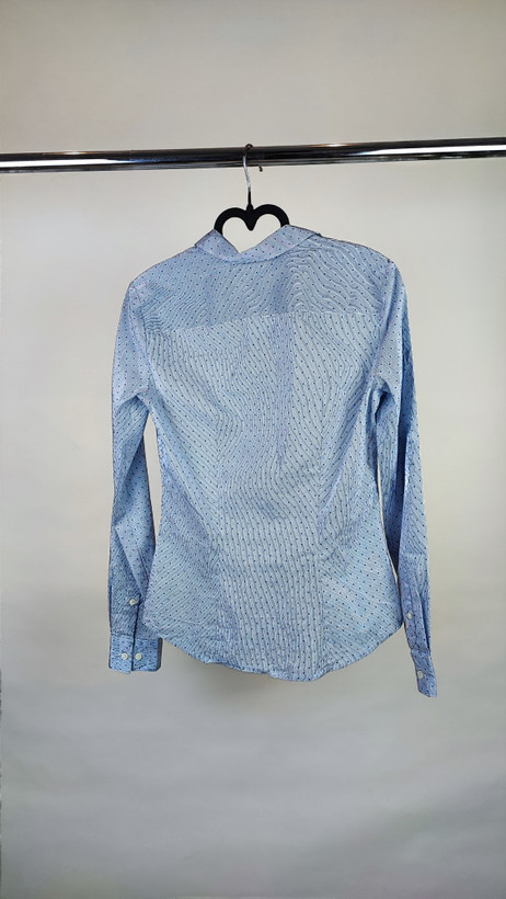 زن با شومیز آبیروشن دکمهدار و یقهبرگردان، آستینبلند و بدون طرح، در پسزمینه روشن ایستاده است