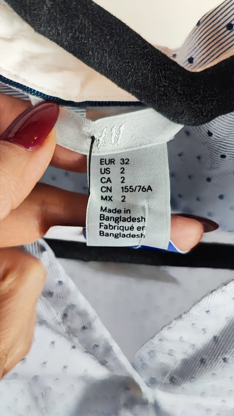 زن با شومیز آبیروشن دکمهدار و یقهبرگردان، آستینبلند و بدون طرح، در پسزمینه روشن ایستاده است