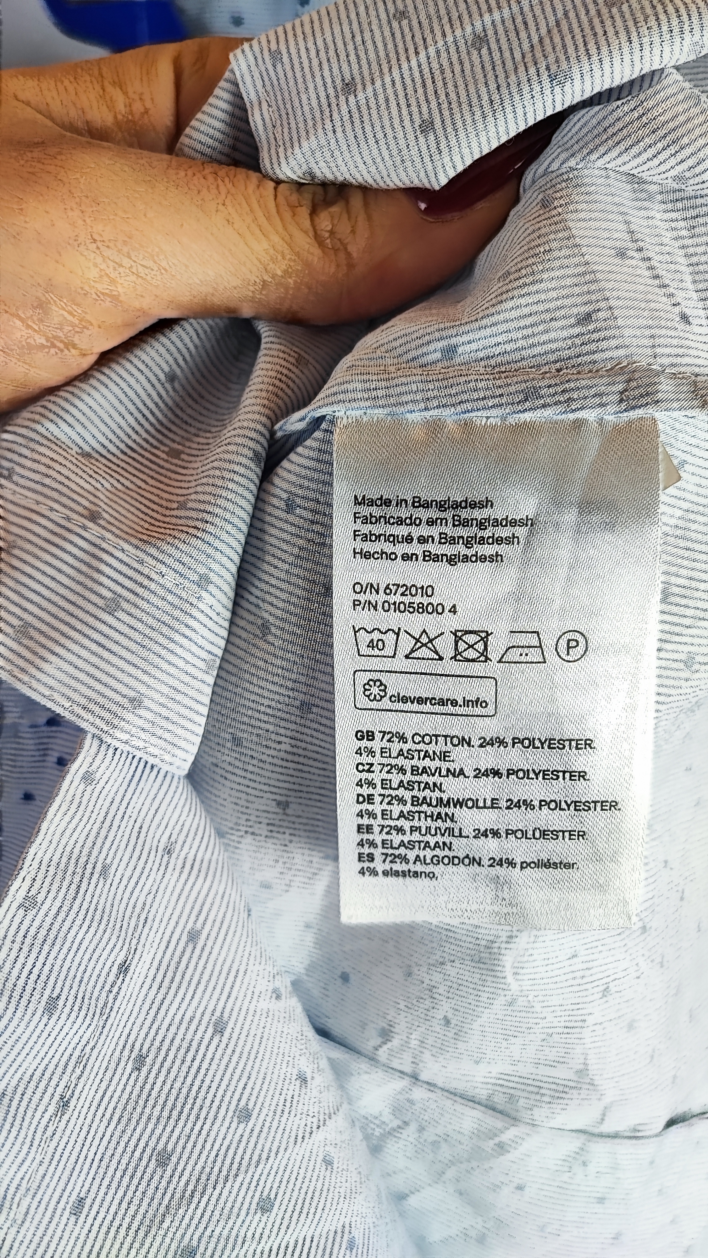 زن با شومیز آبی‌روشن دکمه‌دار و یقه‌برگردان، آستین‌بلند و بدون طرح، در پس‌زمینه روشن ایستاده است