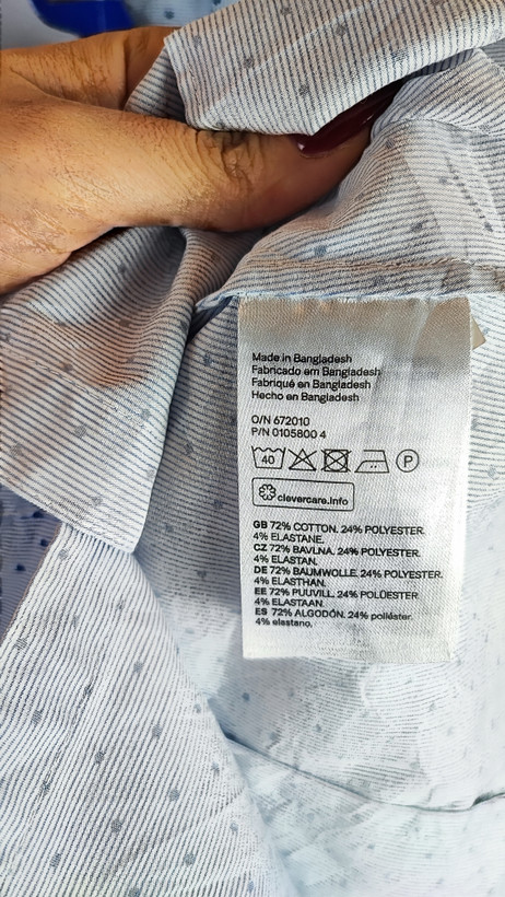 زن با شومیز آبیروشن دکمهدار و یقهبرگردان، آستینبلند و بدون طرح، در پسزمینه روشن ایستاده است