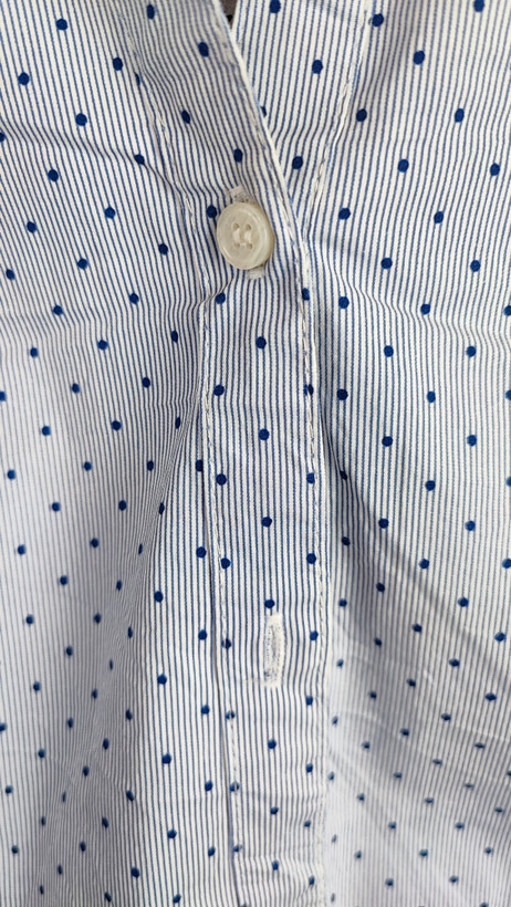 زن با شومیز آبیروشن دکمهدار و یقهبرگردان، آستینبلند و بدون طرح، در پسزمینه روشن ایستاده است