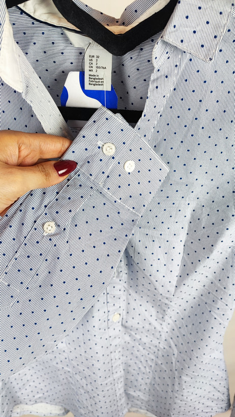 زن با شومیز آبیروشن دکمهدار و یقهبرگردان، آستینبلند و بدون طرح، در پسزمینه روشن ایستاده است