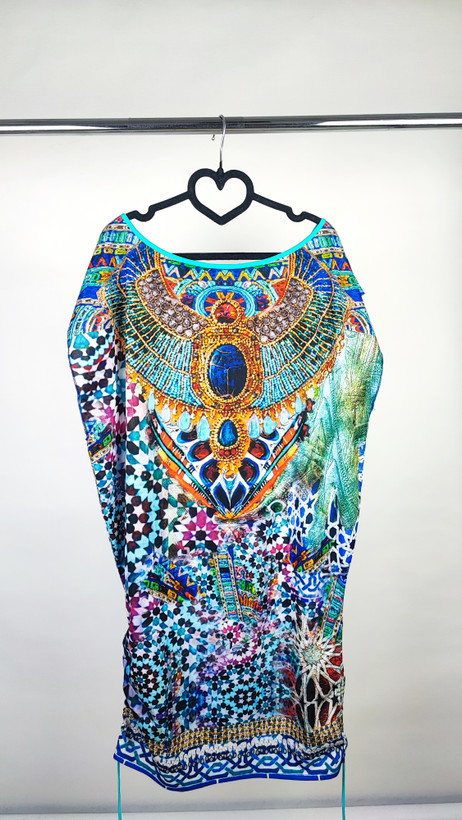 زن با پیراهن کوتاه طرحدار چندرنگ با آستین کوتاه و قد تا بالای زانو در پسزمینه روشن ایستاده است.»