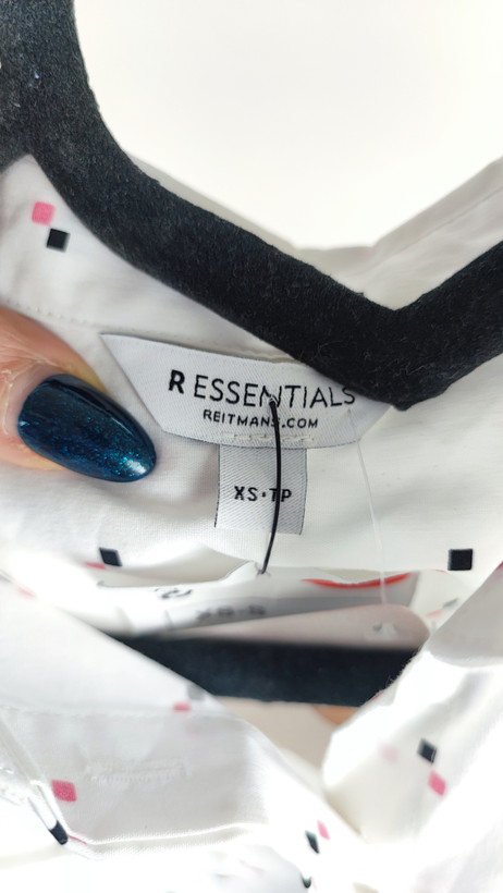 زن ایستاده با شومیز سفید آستینکوتاه و یقهدار، همراه با شلوار جین روشن در پسزمینه ساده.»