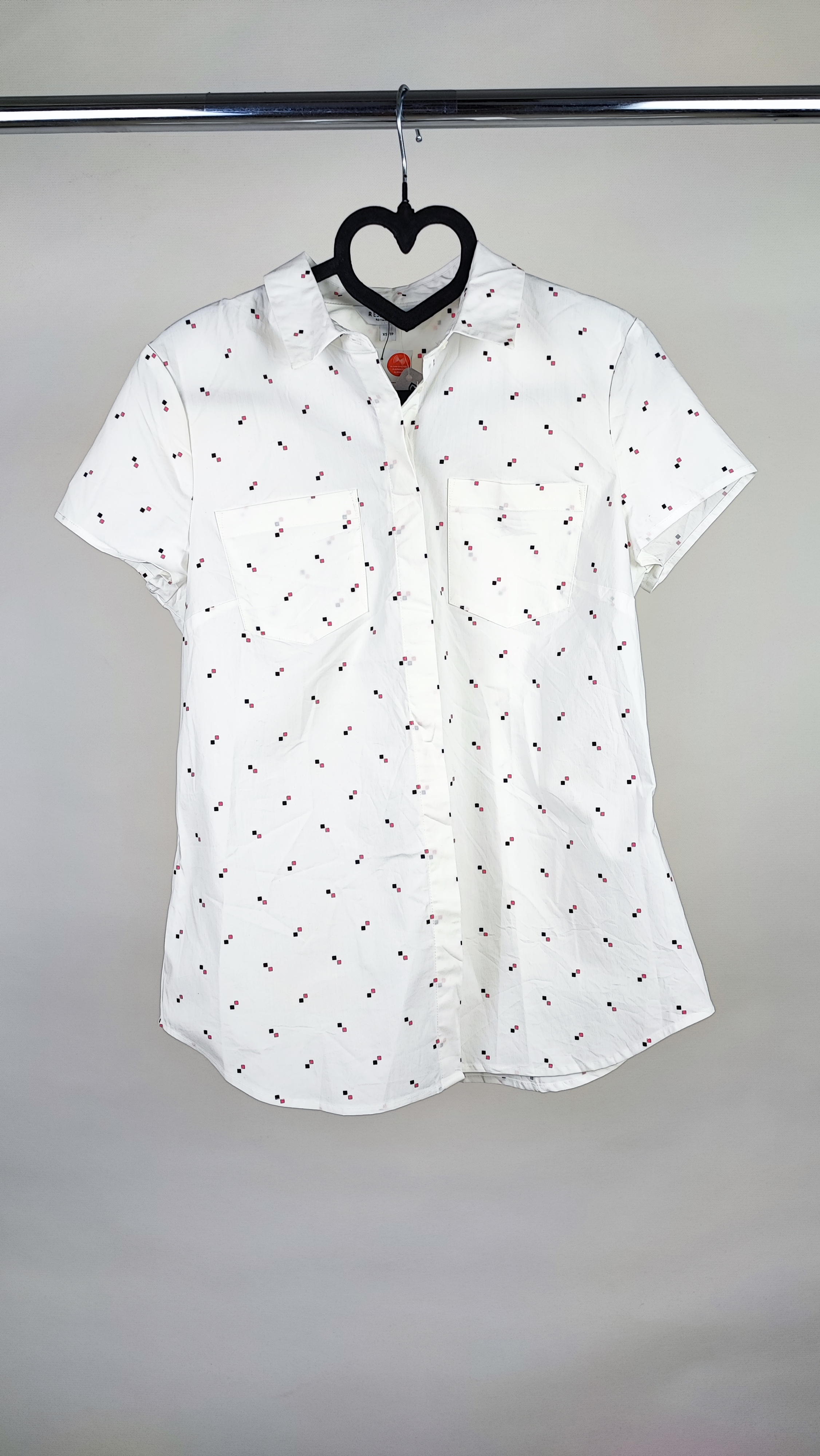 زن ایستاده با شومیز سفید آستین‌کوتاه و یقه‌دار، همراه با شلوار جین روشن در پس‌زمینه ساده.»