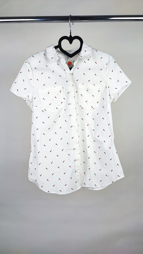 زن ایستاده با شومیز سفید آستینکوتاه و یقهدار، همراه با شلوار جین روشن در پسزمینه ساده.»