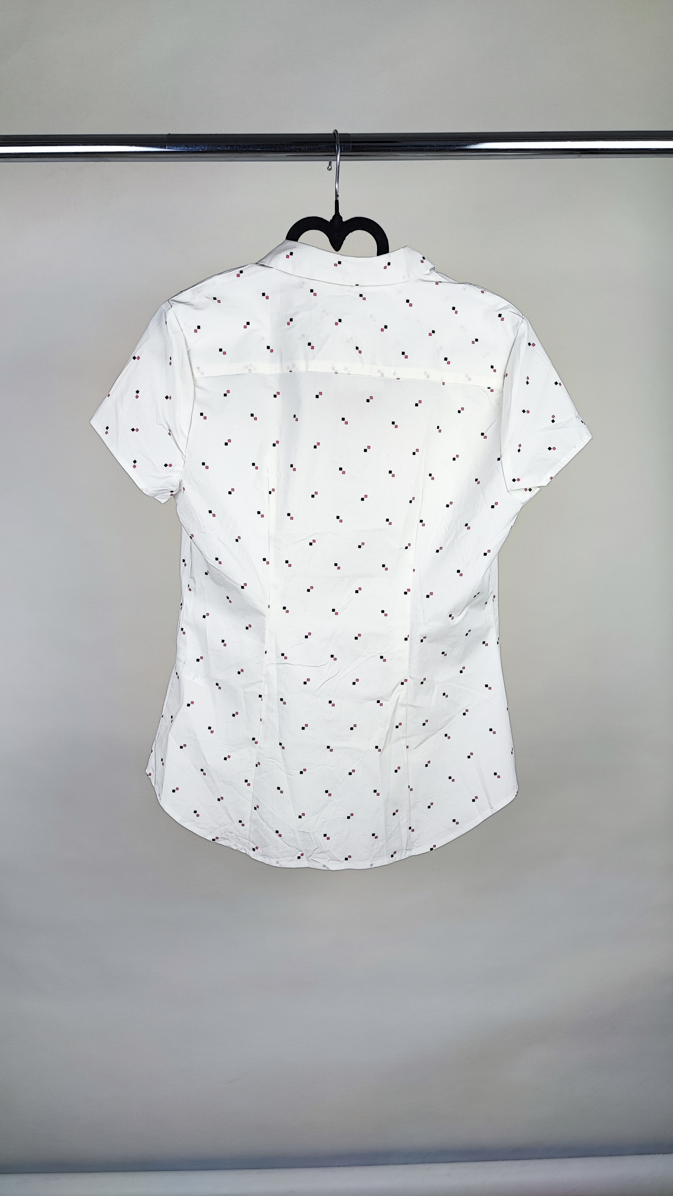 زن ایستاده با شومیز سفید آستین‌کوتاه و یقه‌دار، همراه با شلوار جین روشن در پس‌زمینه ساده.»