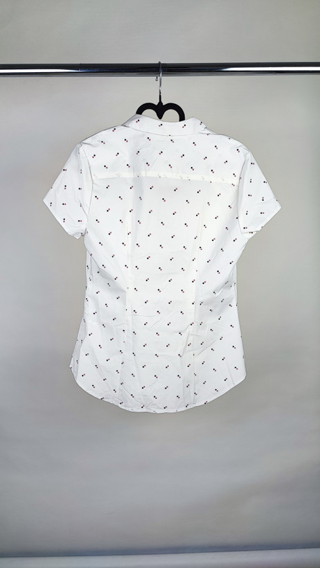 زن ایستاده با شومیز سفید آستینکوتاه و یقهدار، همراه با شلوار جین روشن در پسزمینه ساده.»