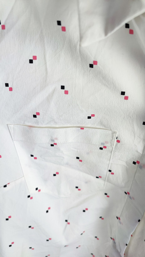 زن ایستاده با شومیز سفید آستینکوتاه و یقهدار، همراه با شلوار جین روشن در پسزمینه ساده.»