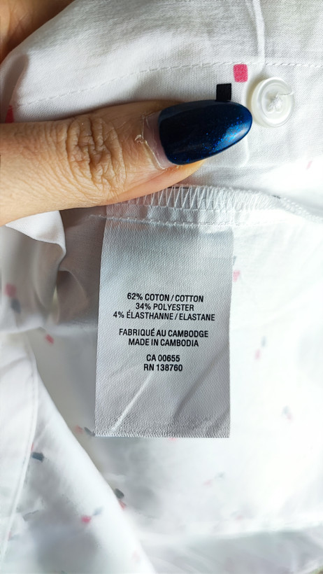 زن ایستاده با شومیز سفید آستینکوتاه و یقهدار، همراه با شلوار جین روشن در پسزمینه ساده.»