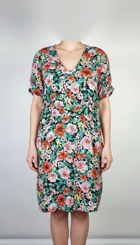 زن ایستاده با پیراهن کوتاه گلدار چندرنگ و یقههفت، آستینکوتاه، در پسزمینه ساده.»