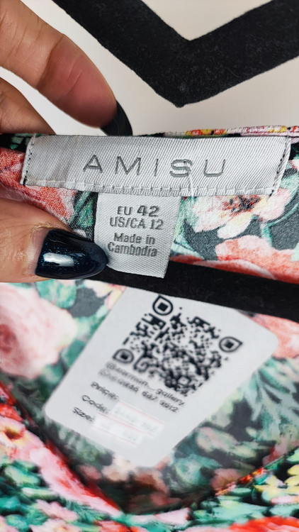 زن ایستاده با پیراهن کوتاه گلدار چندرنگ و یقههفت، آستینکوتاه، در پسزمینه ساده.»