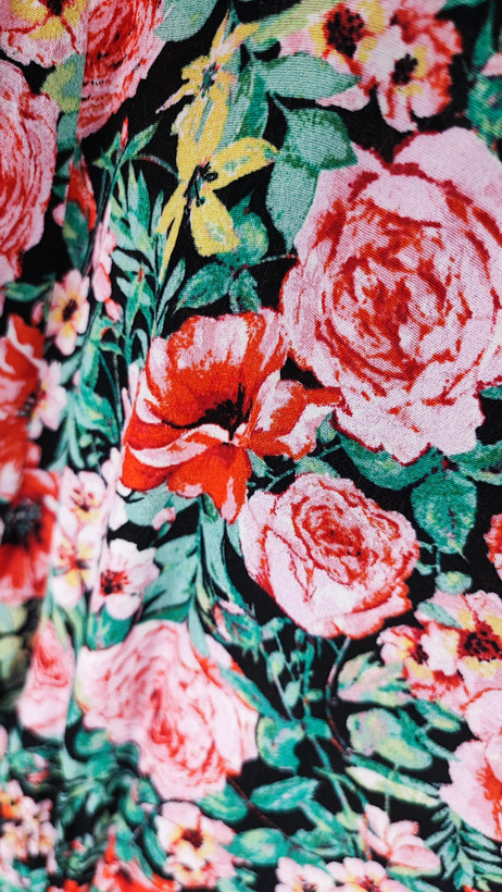 زن ایستاده با پیراهن کوتاه گلدار چندرنگ و یقههفت، آستینکوتاه، در پسزمینه ساده.»