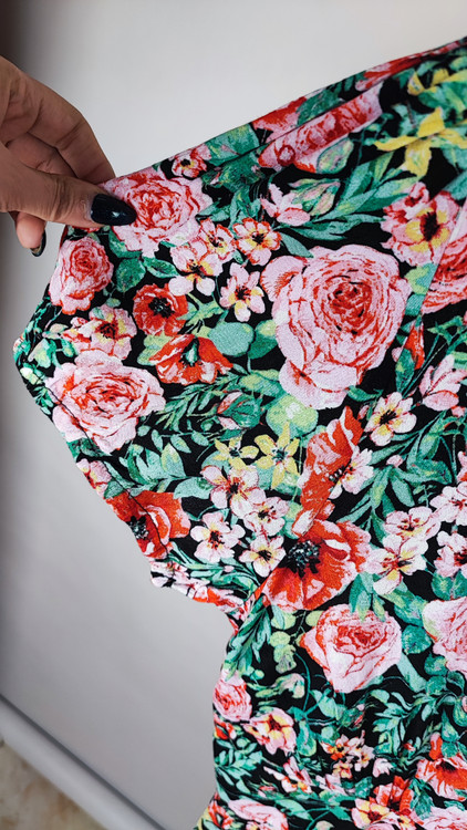 زن ایستاده با پیراهن کوتاه گلدار چندرنگ و یقههفت، آستینکوتاه، در پسزمینه ساده.»