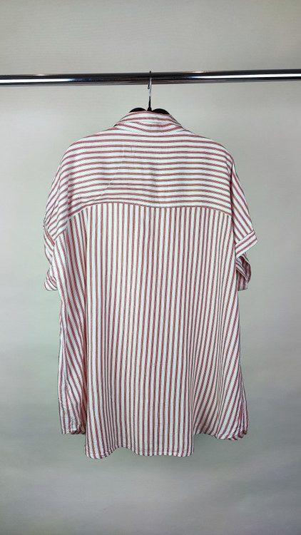 زن سایزبزرگ با شومیز راهراه روشن آستینکوتاه و یقهدار در پسزمینه ساده.»