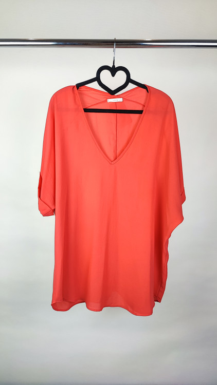 زن سایزبزرگ با شومیز آزاد یقههفت کوتاهآستین به رنگ گلبهی در پسزمینه ساده.»