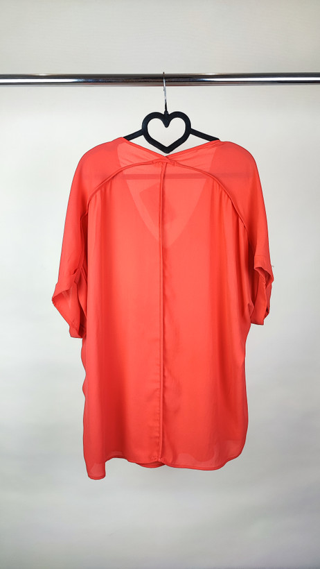 زن سایزبزرگ با شومیز آزاد یقههفت کوتاهآستین به رنگ گلبهی در پسزمینه ساده.»