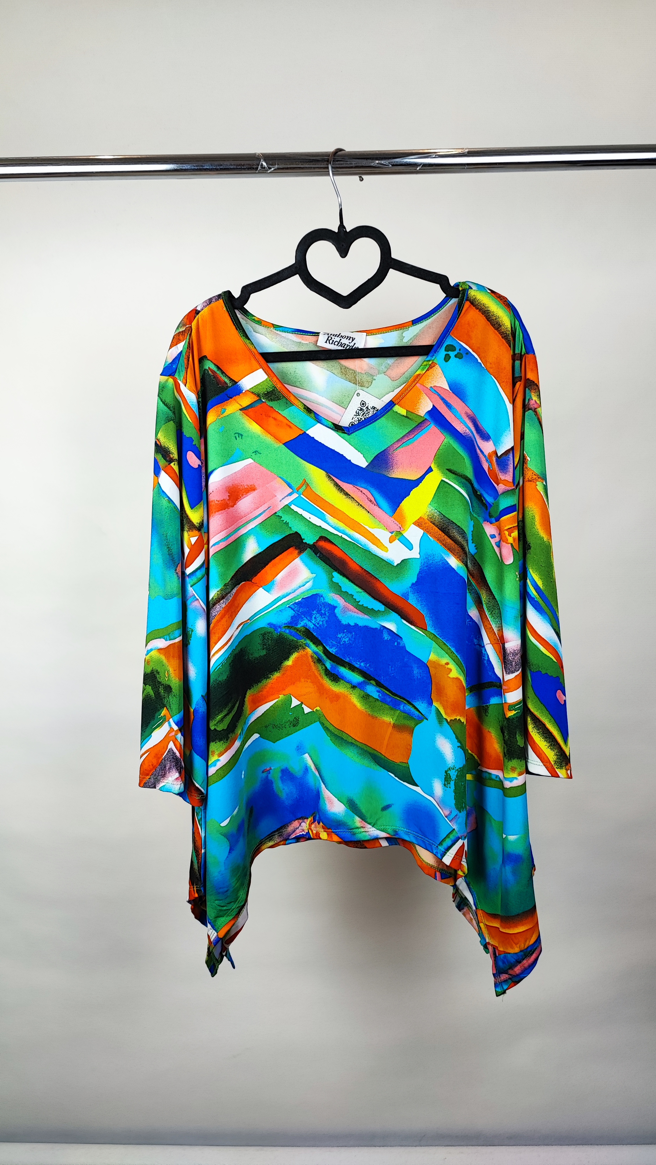 بلوز زنانه سایز بزرگ با طرح رنگارنگ آبی، نارنجی و سبز، آستین‌بلند، روی تن مانکن با شلوار جین تیره در پس‌زمینه روشن.»