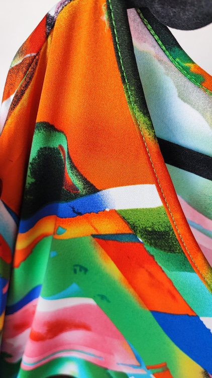 بلوز زنانه سایز بزرگ با طرح رنگارنگ آبی، نارنجی و سبز، آستینبلند، روی تن مانکن با شلوار جین تیره در پسزمینه روشن.»