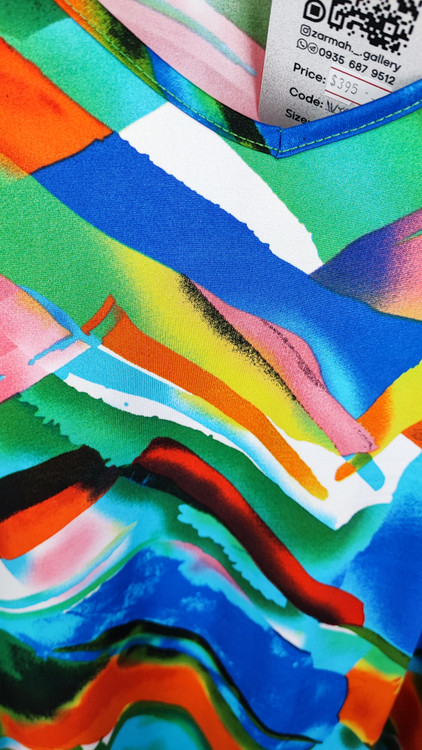 بلوز زنانه سایز بزرگ با طرح رنگارنگ آبی، نارنجی و سبز، آستینبلند، روی تن مانکن با شلوار جین تیره در پسزمینه روشن.»