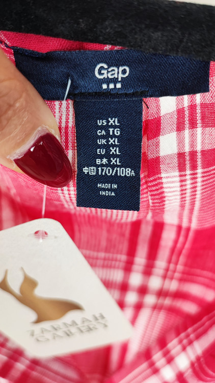 تاپ زنانه سایز بزرگ چهارخونه صورتی و قرمز، بدون آستین با گره جلو، روی تن مانکن با شلوار تیره در پسزمینه روشن.»