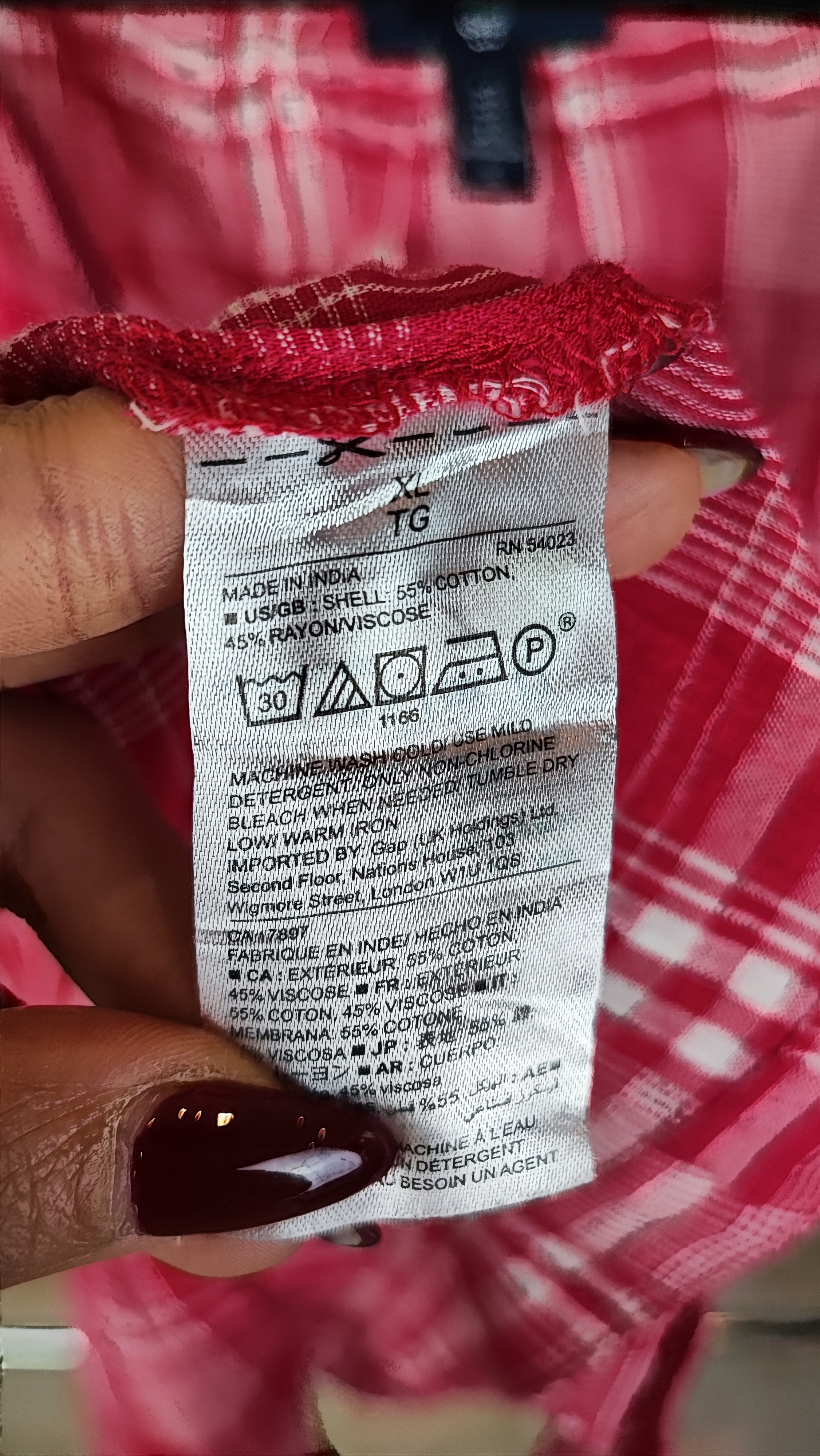 تاپ زنانه سایز بزرگ چهارخونه صورتی و قرمز، بدون آستین با گره جلو، روی تن مانکن با شلوار تیره در پس‌زمینه روشن.»