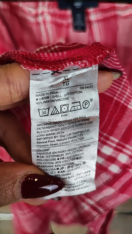 تاپ زنانه سایز بزرگ چهارخونه صورتی و قرمز، بدون آستین با گره جلو، روی تن مانکن با شلوار تیره در پسزمینه روشن.»