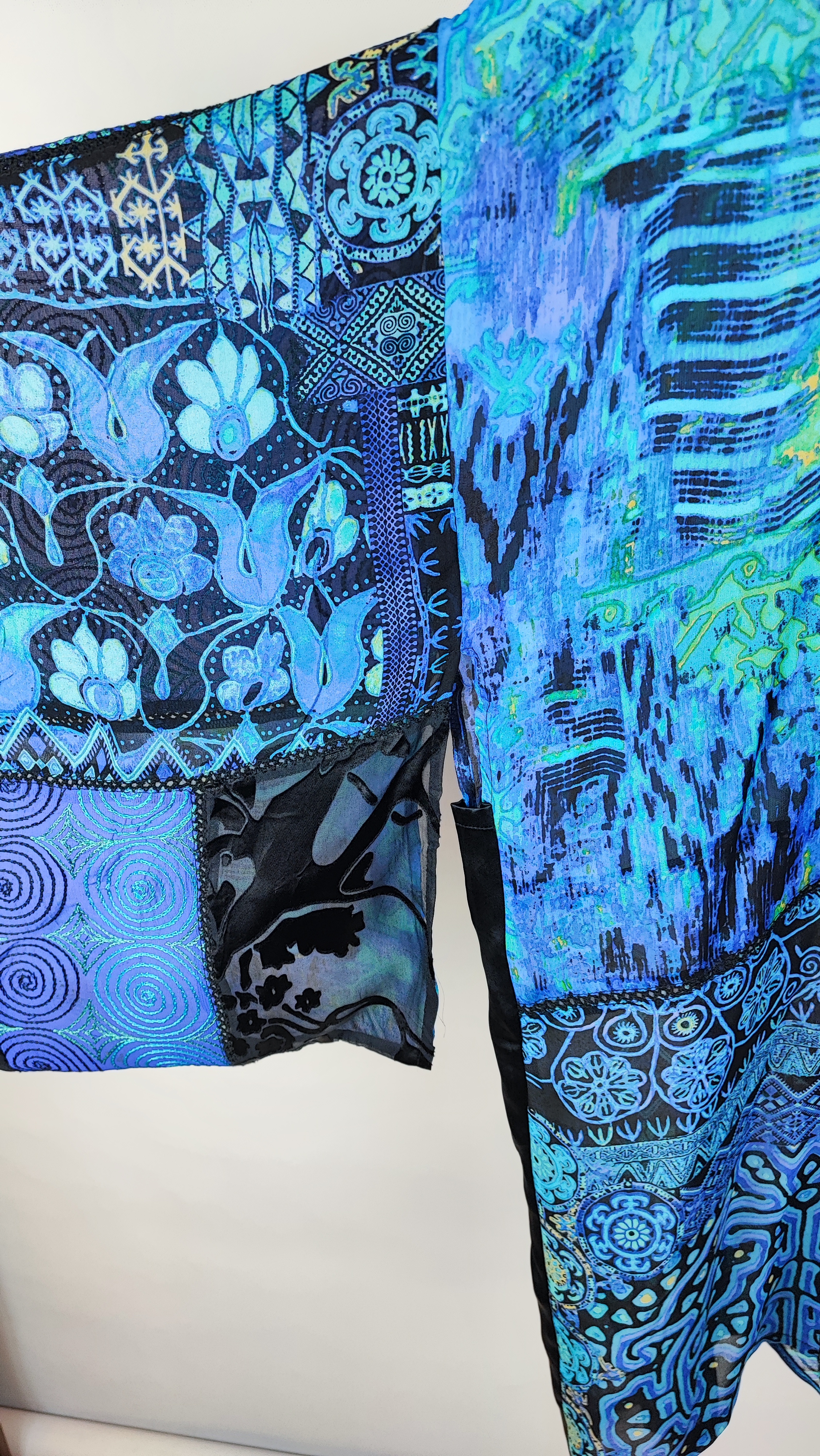 رویه شومیز زنانه فری‌سایز با ترکیب رنگ آبی‑سبز، آستین آزاد و فرم کِپ، روی تاپ مشکی، در پس‌زمینه روشن.»