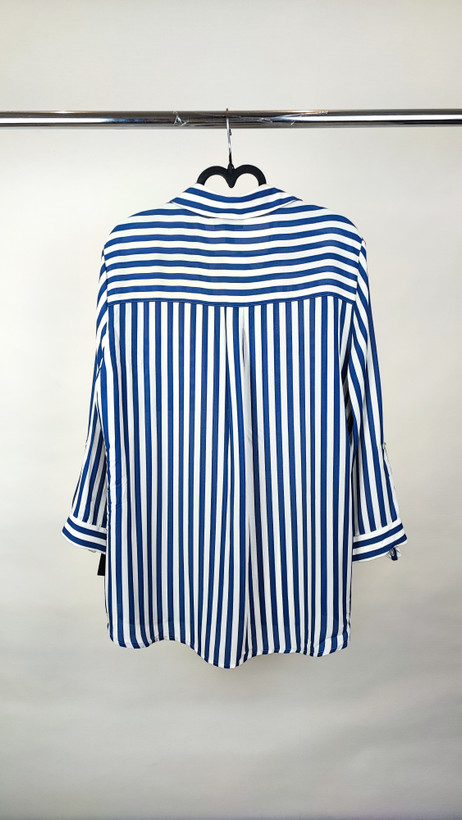 شومیز زنانه آبی راهراه سایز بزرگ با آستین بلند و مدل آزاد، روی تن مانکن با شلوار تیره، پسزمینه روشن.»