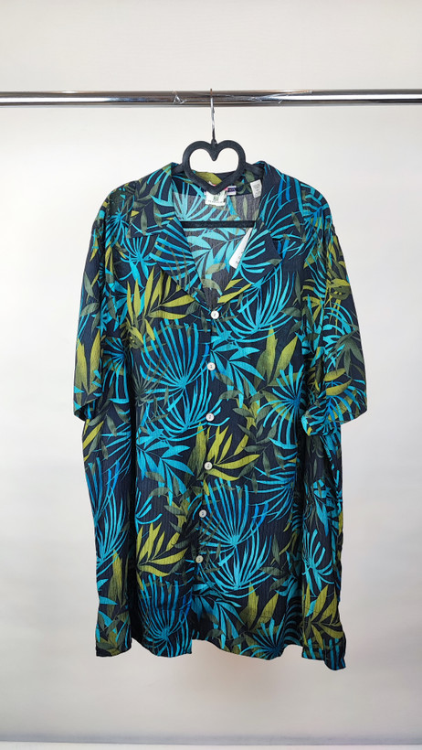 شومیز زنانه سایز بزرگ با زمینه سبزآبی و طرح گلهای زرد و نارنجی، آستین کوتاه و فرم آزاد روی تن مانکن، پسزمینه روشن.»