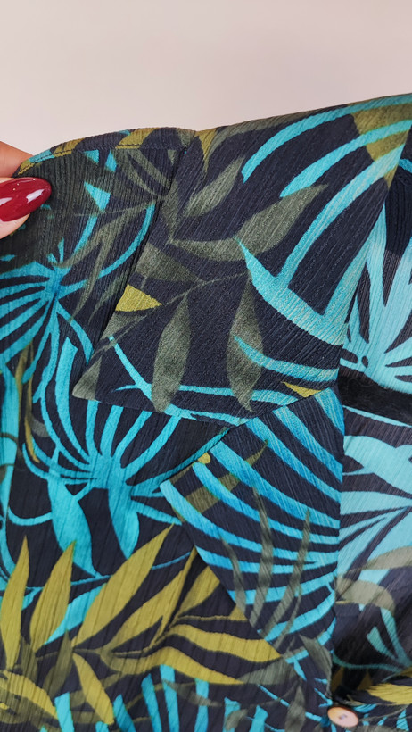 شومیز زنانه سایز بزرگ با زمینه سبزآبی و طرح گلهای زرد و نارنجی، آستین کوتاه و فرم آزاد روی تن مانکن، پسزمینه روشن.»