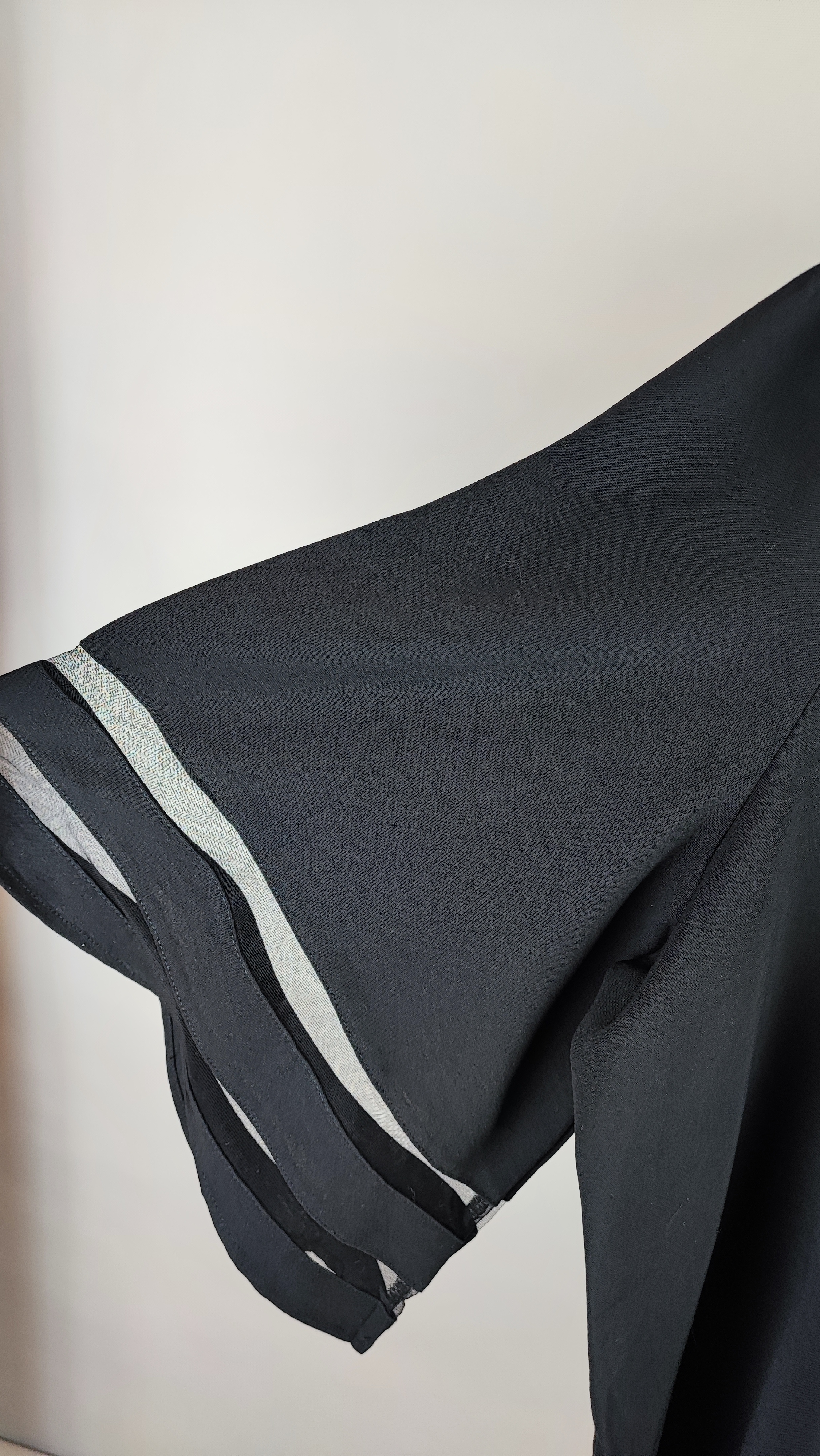 شومیز زنانه مشکی سایز بزرگ با آستین سه‌ربع و نوارهای تزیینی روی آستین، روی تن مانکن، پس‌زمینه روشن.