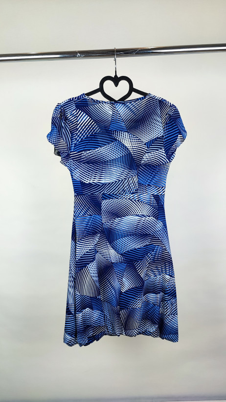 پیراهن زنانه استوک آبی طرحدار، آستین کوتاه، یقه ساده، قد بالای زانو، فرم مرتب و راحت، مناسب استایل روزمره، ایستاده روی مدل با پسزمینه روشن.