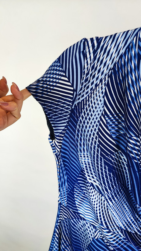 پیراهن زنانه استوک آبی طرحدار، آستین کوتاه، یقه ساده، قد بالای زانو، فرم مرتب و راحت، مناسب استایل روزمره، ایستاده روی مدل با پسزمینه روشن.