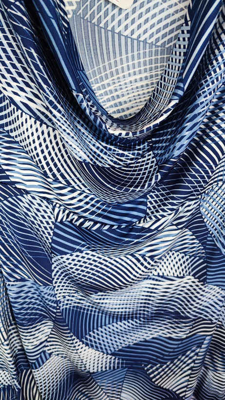 پیراهن زنانه استوک آبی طرحدار، آستین کوتاه، یقه ساده، قد بالای زانو، فرم مرتب و راحت، مناسب استایل روزمره، ایستاده روی مدل با پسزمینه روشن.