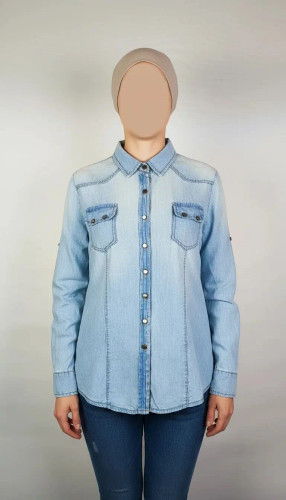 شومیز جین زنانه استوک آبی روشن، آستین بلند، یقه کلاسیک، فرم مرتب و کاربردی، مناسب استایل روزمره، ایستاده روی مدل با پسزمینه روشن.