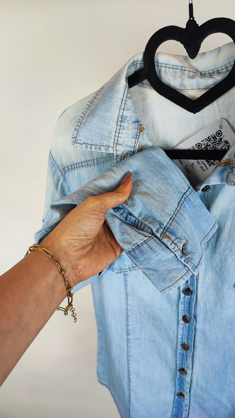 شومیز جین زنانه استوک آبی روشن، آستین بلند، یقه کلاسیک، فرم مرتب و کاربردی، مناسب استایل روزمره، ایستاده روی مدل با پسزمینه روشن.