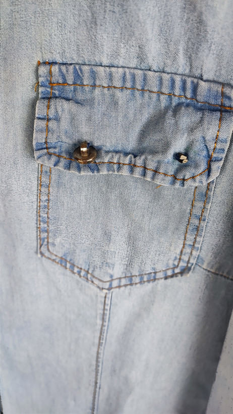 شومیز جین زنانه استوک آبی روشن، آستین بلند، یقه کلاسیک، فرم مرتب و کاربردی، مناسب استایل روزمره، ایستاده روی مدل با پسزمینه روشن.