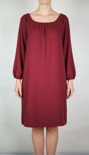 پیراهن زنانه استوک زرشکی، آستینبلند با یقه گرد باز، قد تا بالای زانو، فرم آزاد و ساده، مناسب استفاده روزمره و نیمهمجلس، ایستاده روی مدل با پسزمینه روشن.