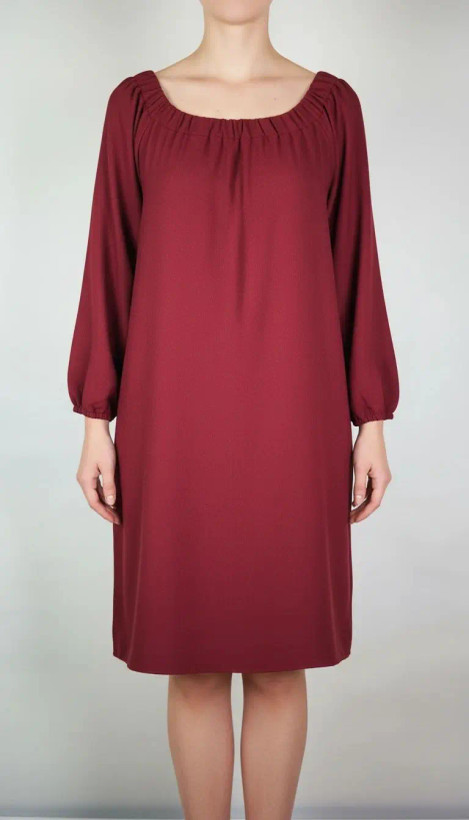 پیراهن زنانه استوک زرشکی، آستینبلند با یقه گرد باز، قد تا بالای زانو، فرم آزاد و ساده، مناسب استفاده روزمره و نیمهمجلس، ایستاده روی مدل با پسزمینه روشن.