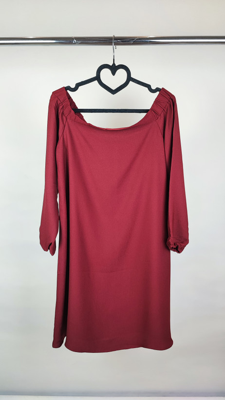 پیراهن زنانه استوک زرشکی، آستینبلند با یقه گرد باز، قد تا بالای زانو، فرم آزاد و ساده، مناسب استفاده روزمره و نیمهمجلس، ایستاده روی مدل با پسزمینه روشن.