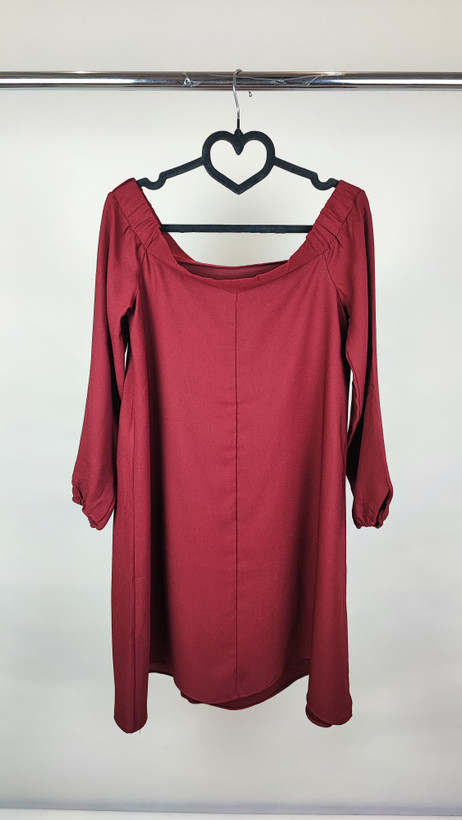 پیراهن زنانه استوک زرشکی، آستینبلند با یقه گرد باز، قد تا بالای زانو، فرم آزاد و ساده، مناسب استفاده روزمره و نیمهمجلس، ایستاده روی مدل با پسزمینه روشن.