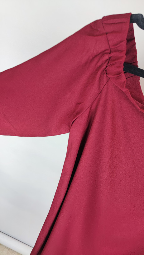 پیراهن زنانه استوک زرشکی، آستینبلند با یقه گرد باز، قد تا بالای زانو، فرم آزاد و ساده، مناسب استفاده روزمره و نیمهمجلس، ایستاده روی مدل با پسزمینه روشن.