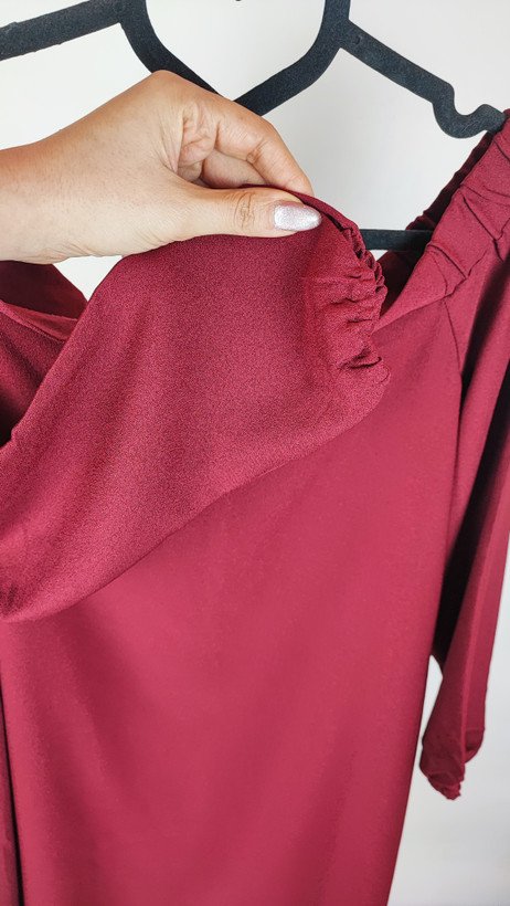 پیراهن زنانه استوک زرشکی، آستینبلند با یقه گرد باز، قد تا بالای زانو، فرم آزاد و ساده، مناسب استفاده روزمره و نیمهمجلس، ایستاده روی مدل با پسزمینه روشن.