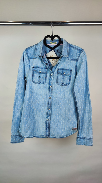 شومیز زنانه جین استوک رنگ آبی روشن، آستین بلند با فرم جذب و یقه کلاسیک، قد کوتاه و تنخور مرتب، ایستاده روی مدل با پسزمینه روشن.