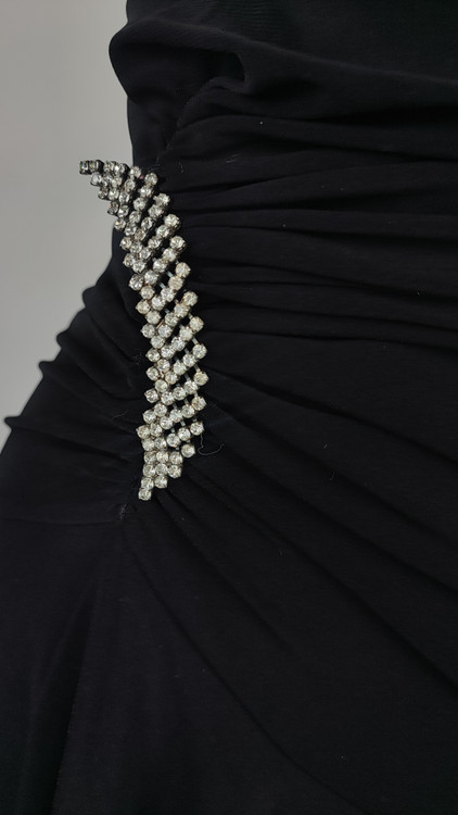 پیراهن زنانه وارداتی استوک مشکی بنددار، یقه هفت، فرم آزاد با پاییندوزی نامتقارن، قد حدود ۹۵ سانتیمتر، مناسب استایل مهمانی و شب، عکاسیشده روی تن با پسزمینه ساده روشن.