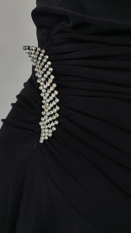 پیراهن زنانه وارداتی استوک مشکی بنددار، یقه هفت، فرم آزاد با پاییندوزی نامتقارن، قد حدود ۹۵ سانتیمتر، مناسب استایل مهمانی و شب، عکاسیشده روی تن با پسزمینه ساده روشن.